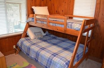 A cozy cabin bedroom with wooden bunk beds featuring blue plaid bedding, set against warm wood-paneled walls, perfect for a family-friendly retreat.