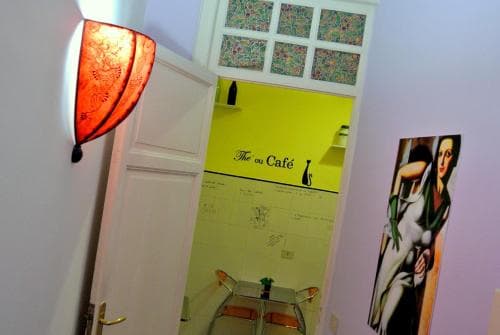 A cozy café entrance features vibrant yellow walls, eclectic decor including a red patterned lamp and an artistic poster, inviting travelers to explore its charming and artistic ambiance.