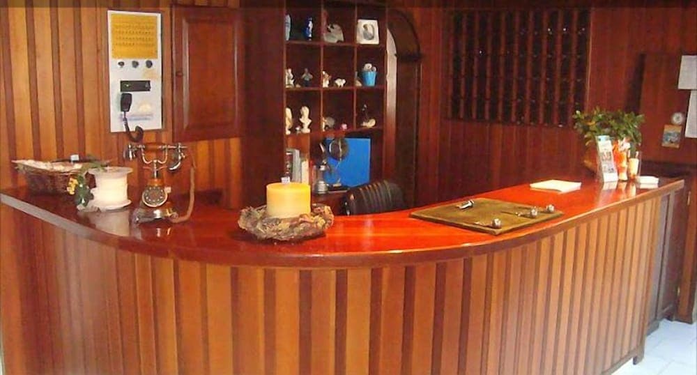 A cozy hotel reception area features warm wooden paneling, a polished counter adorned with a candle and vintage telephone, creating an inviting atmosphere ideal for travelers seeking a charming check-in experience.