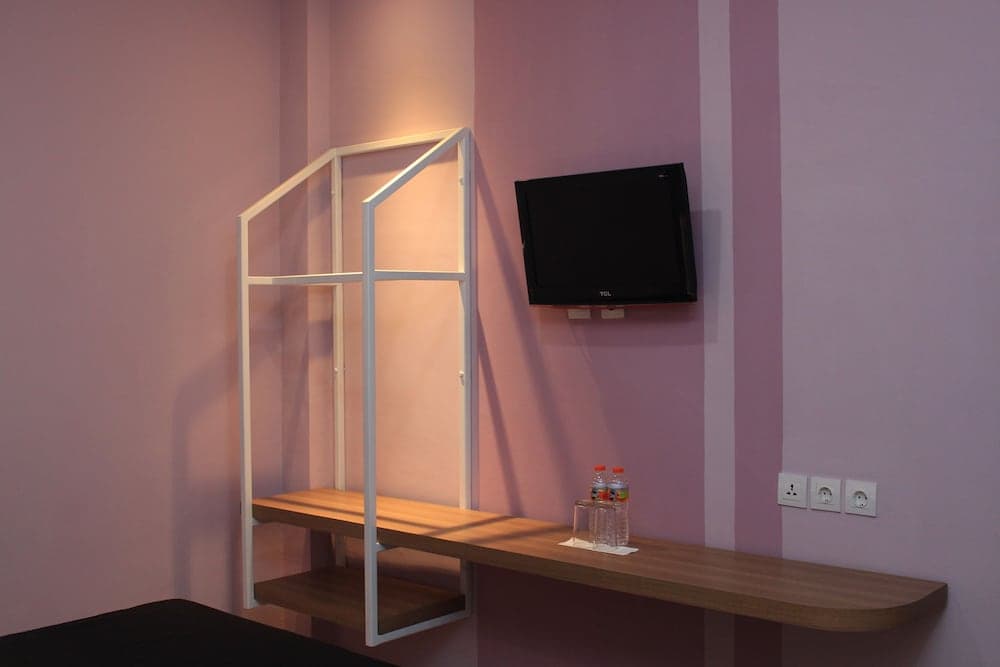 A cozy hotel room corner features a minimalist desk with a geometric frame, a mounted TV, and water bottles on the shelf, ideal for travelers seeking a modern and functional space.