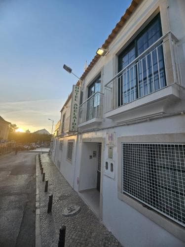 A serene evening view of a quaint hotel with white walls, balconies, and tiled roofs along a cobblestone street, ideal for travelers seeking a peaceful European getaway.