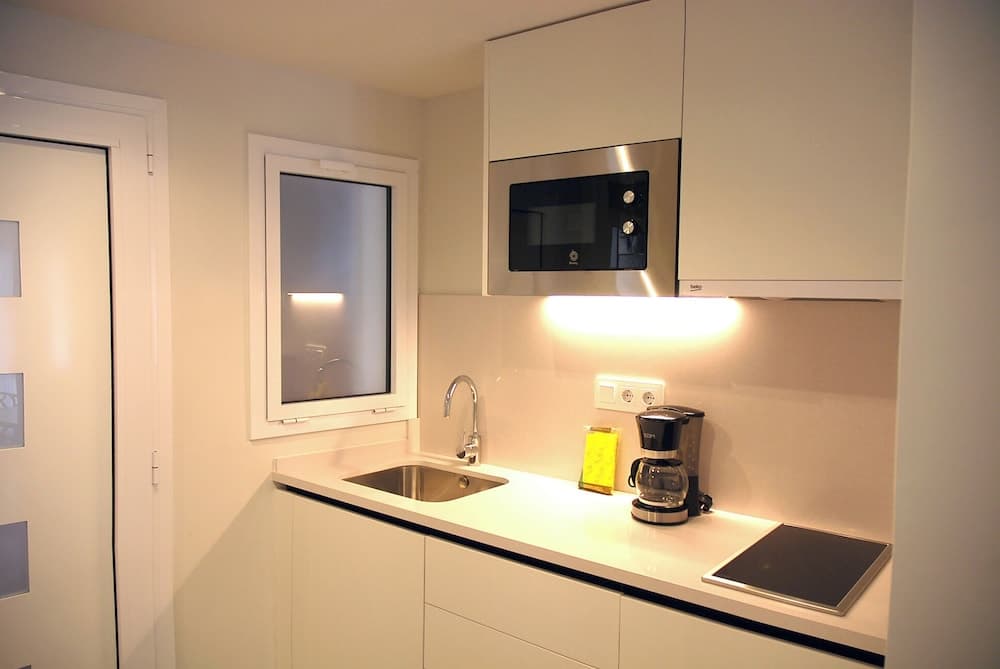 A cozy, modern kitchenette features sleek white cabinetry, a stainless steel sink, a built-in microwave, and a coffee maker, ideal for travelers seeking a compact yet functional cooking space in their accommodation.