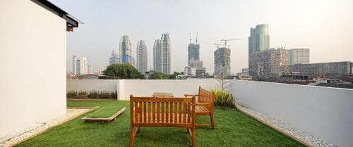A serene rooftop garden with lush green grass, wooden benches, and a city skyline backdrop offers a tranquil urban retreat for travelers seeking relaxation amidst skyscrapers.