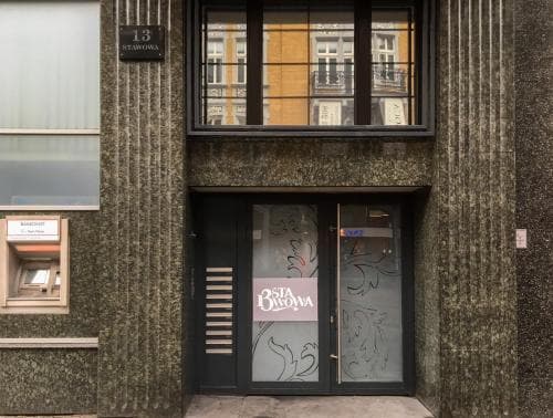 A modern urban storefront with a textured facade, large windows reflecting nearby buildings, and a glass door featuring "Dista Browa" signage, ideal for travelers seeking local businesses in a cityscape setting.