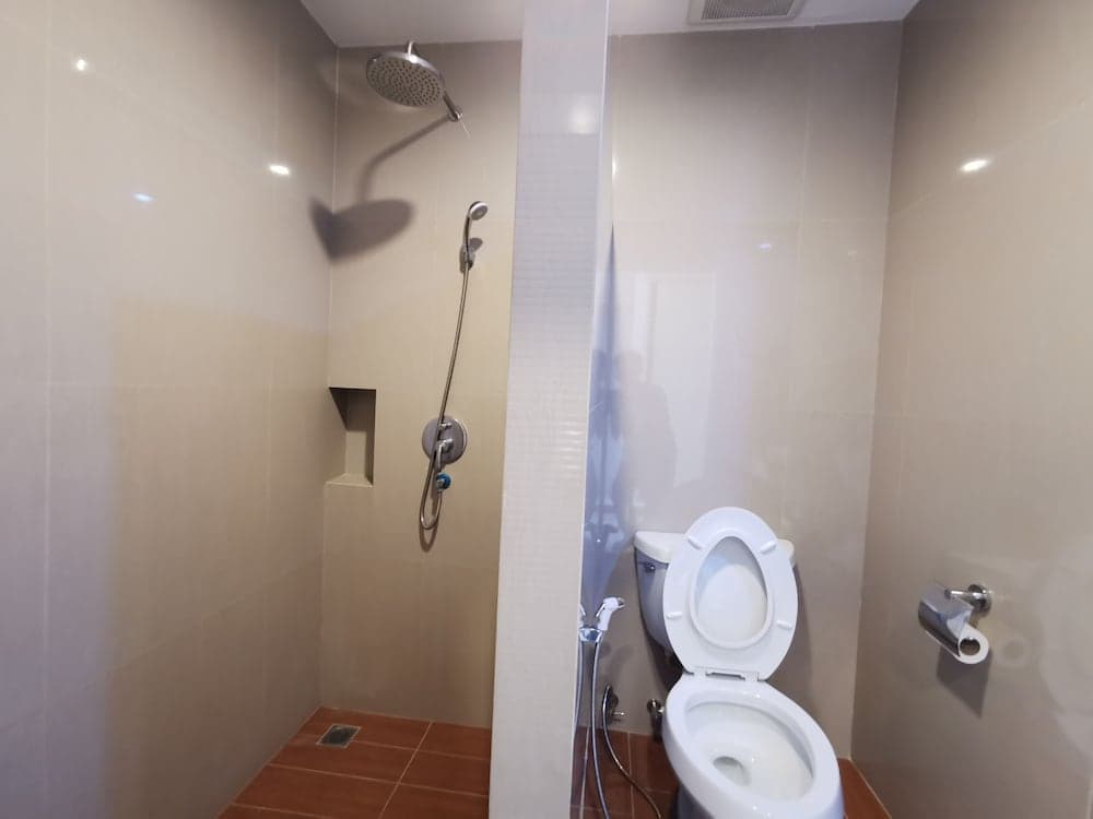 A clean, modern bathroom with beige tiles, a shower with a handheld attachment, a toilet, and a frosted glass partition creates a functional and serene space ideal for travelers seeking comfort in accommodations.