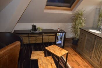 A cozy attic lounge with wooden furniture, striped carpeting, and potted plants creates an intimate atmosphere ideal for travelers seeking a unique accommodation experience.