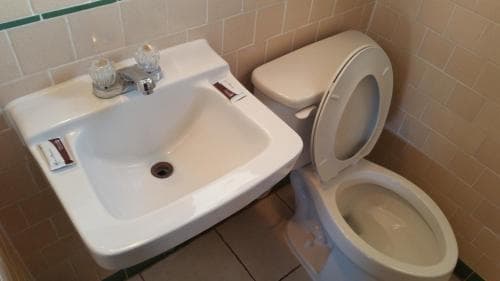 A clean, tiled bathroom featuring a white sink with a soap dispenser and a toilet, ideal for travelers seeking basic hygiene facilities in a compact space.
