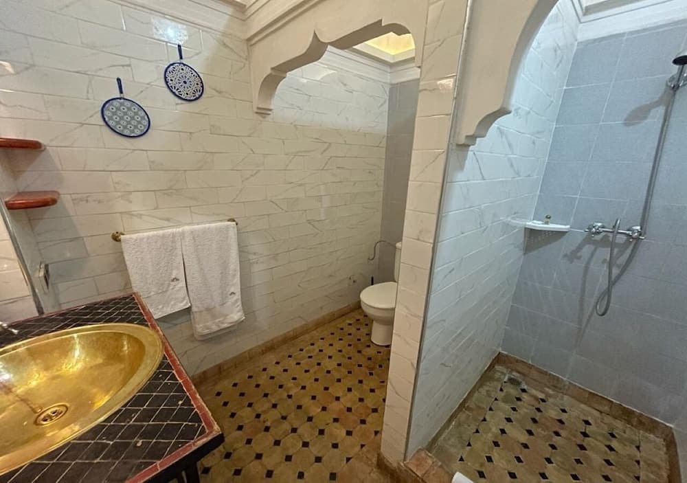 A serene Moroccan-style bathroom features intricate tilework, a golden sink, and arched doorways, ideal for travelers seeking a luxurious and culturally immersive experience.