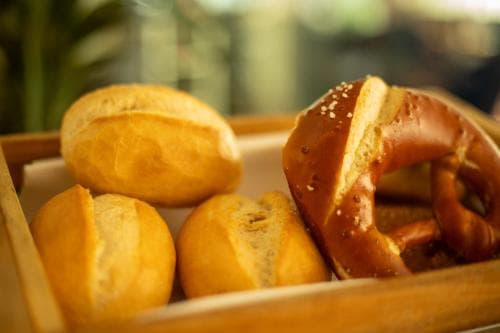 A cozy café scene featuring fresh bread rolls and a pretzel in a wooden tray, evoking warmth and comfort, perfect for travelers seeking local culinary delights.