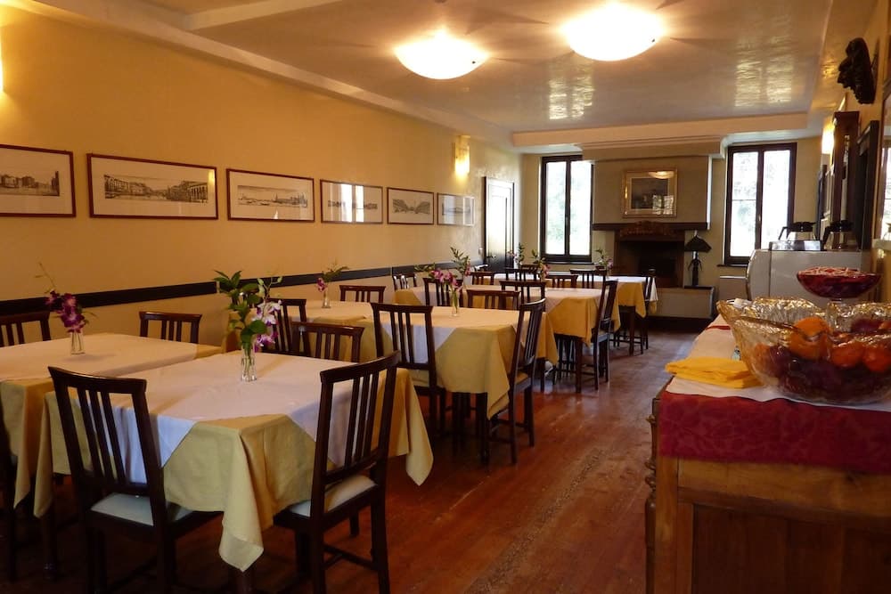 A cozy indoor dining area with wooden floors, neatly arranged tables draped in yellow and white linens, framed artwork on the walls, and a warm ambiance ideal for travelers seeking a comfortable restaurant experience.