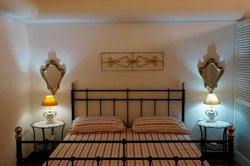 A cozy bedroom with a classic iron bed, ornate wall mirrors, and warm bedside lamps creates an inviting atmosphere ideal for travelers seeking a charming and comfortable stay.