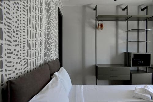 A cozy hotel room features a neatly made bed beside a patterned wall and sleek shelving unit, creating a modern and inviting atmosphere ideal for travelers seeking comfort and style.