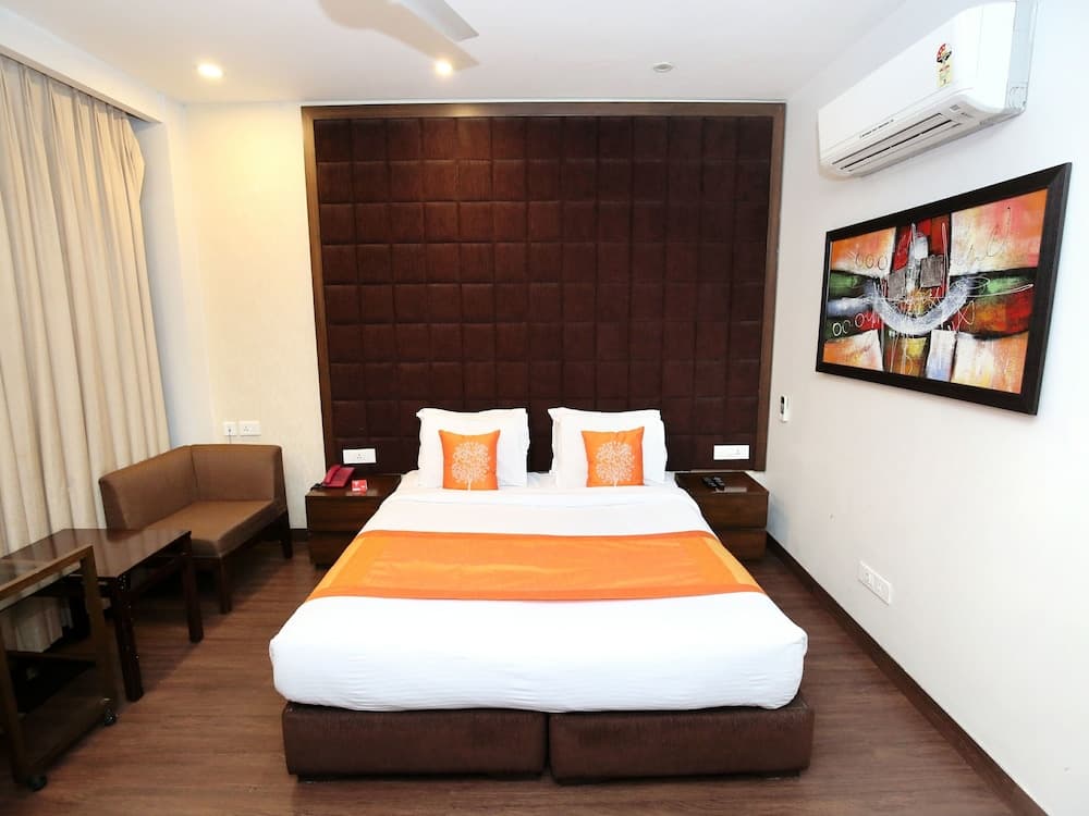 A cozy hotel room features a neatly made bed with orange accents, a textured brown headboard, a small seating area, and vibrant wall art, ideal for travelers seeking comfort and style.