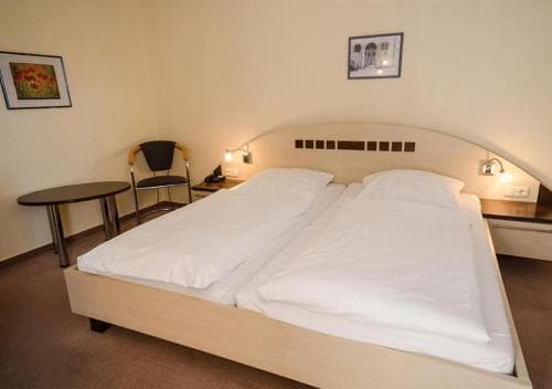 A cozy hotel room features two neatly made beds under soft lighting, framed artwork on the walls, and a small seating area, ideal for travelers seeking comfort and simplicity.