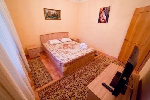 A cozy hotel room features a neatly made bed adorned with patterned bedding, warm-toned walls decorated with art, a wooden desk with a computer, and a vibrant rug, ideal for travelers seeking comfort and functionality.