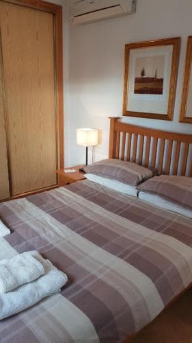 A cozy hotel room features a neatly made bed with plaid bedding, wooden furnishings, and framed artwork, creating a warm and inviting atmosphere ideal for travelers seeking comfort and relaxation.