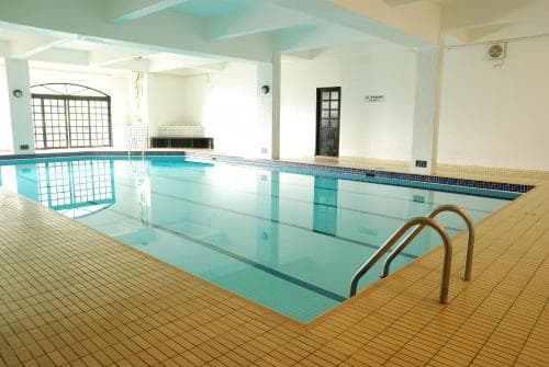 A serene indoor swimming pool with clear blue water, tiled floors, and large windows offers a tranquil setting ideal for relaxation and fitness activities.