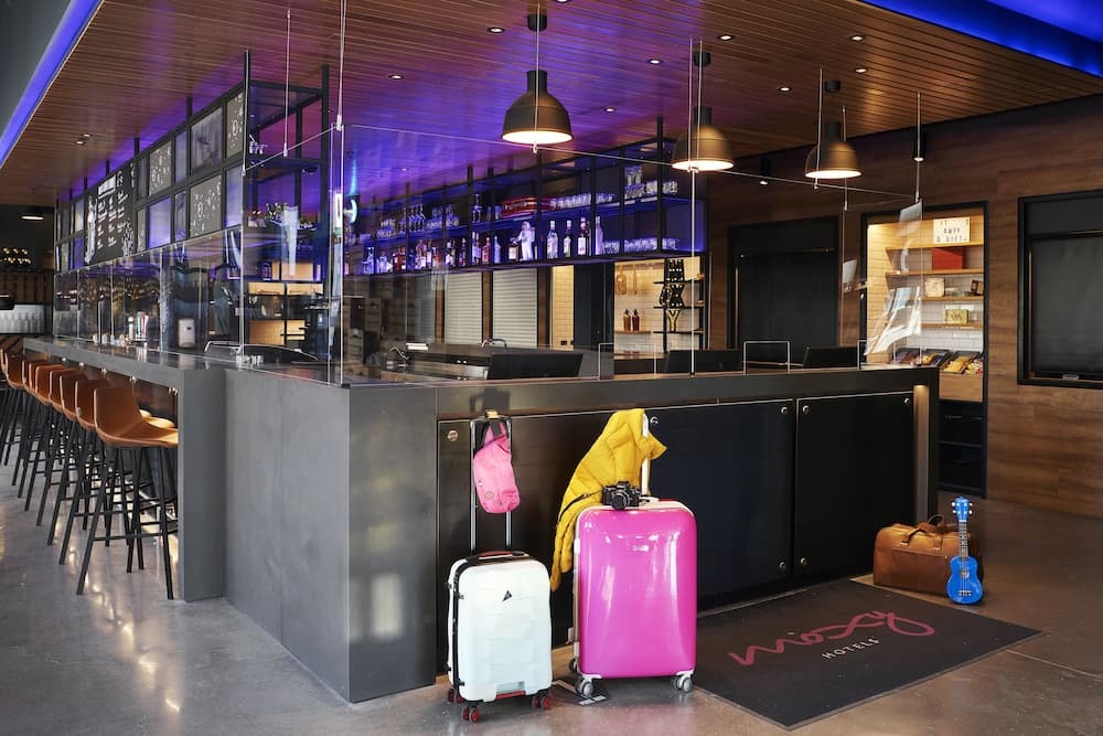 A modern hotel lobby with sleek bar seating, vibrant lighting, and colorful luggage creates an inviting atmosphere ideal for travelers seeking a stylish urban retreat.