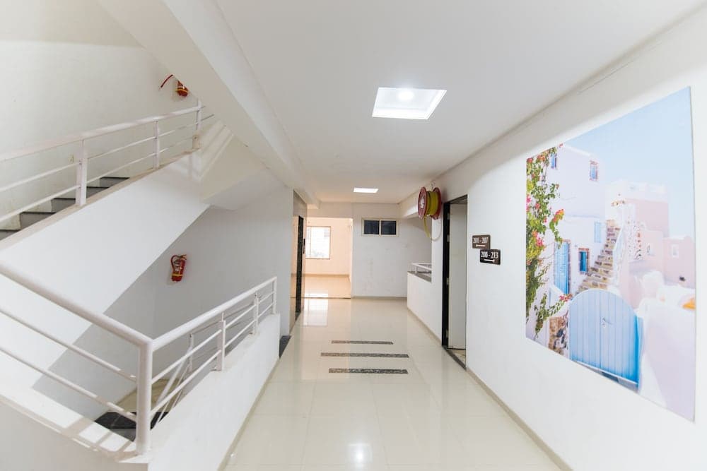 A bright, modern hotel corridor features white tiled floors, a staircase, safety equipment, and a large mural of a Mediterranean scene, ideal for travelers seeking a clean and inviting accommodation experience.