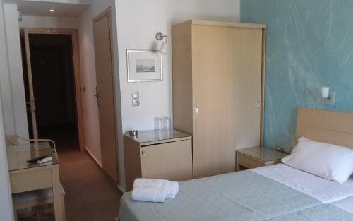 A cozy hotel room features a neatly made bed, wooden furniture, and a small desk, creating a comfortable and functional space ideal for travelers seeking simplicity and convenience.