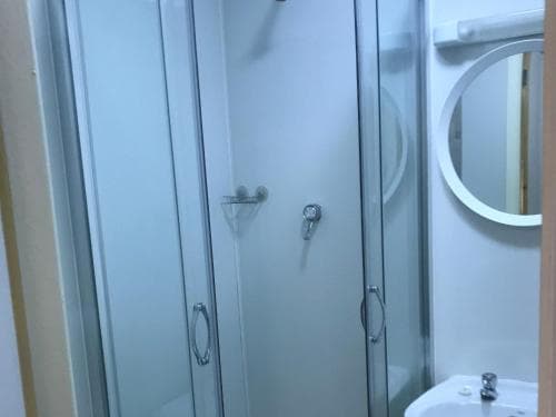 A modern bathroom featuring a glass-enclosed shower, round mirror, and sleek fixtures exudes cleanliness and simplicity, ideal for travelers seeking a comfortable stay in a compact space.