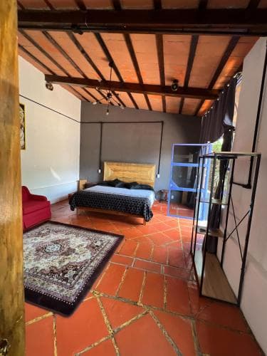 A cozy rustic bedroom with terracotta tiled floors, exposed wooden beams, and eclectic furnishings creates an inviting atmosphere ideal for travelers seeking a unique and charming accommodation experience.
