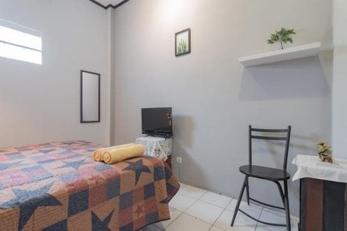 A cozy, minimalist bedroom with a patterned bedspread, small TV, chair, and simple decor creates a serene atmosphere ideal for budget travelers seeking comfort in compact spaces.