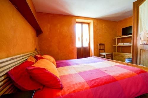 A cozy bedroom with warm orange walls, wooden beams, and vibrant red bedding invites travelers seeking comfort in a rustic retreat.