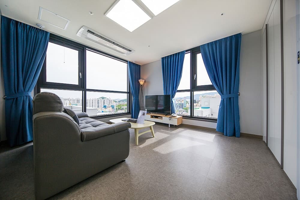 A modern living room with large windows, blue curtains, and a cozy sofa offers a serene cityscape view, ideal for travelers seeking a comfortable urban retreat.
