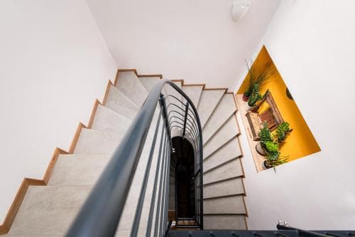 A modern staircase with a sleek black railing ascends through a minimalist interior, complemented by a vibrant yellow wall niche adorned with green plants, ideal for travelers seeking contemporary design inspiration in urban accommodations.