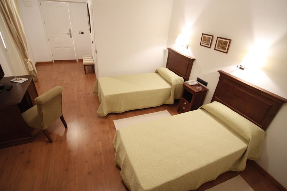 A cozy hotel room with two neatly made single beds, wooden flooring, soft lighting, and simple decor offers a comfortable stay for travelers seeking relaxation.