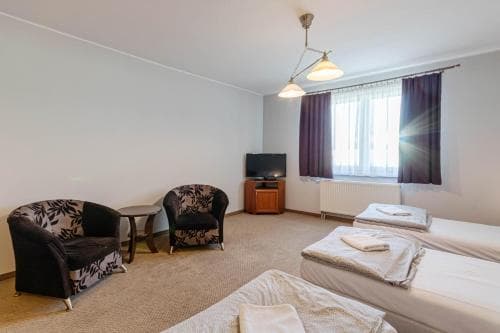 A cozy hotel room with two neatly made beds, patterned armchairs, a small TV on a wooden stand, and a window with curtains letting in soft sunlight, ideal for travelers seeking comfort and simplicity.