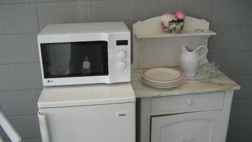 A cozy kitchenette scene featuring a microwave atop a washing machine beside a vintage cabinet with plates and a pitcher, evoking a quaint, homey atmosphere ideal for budget-friendly accommodations or rustic retreats.