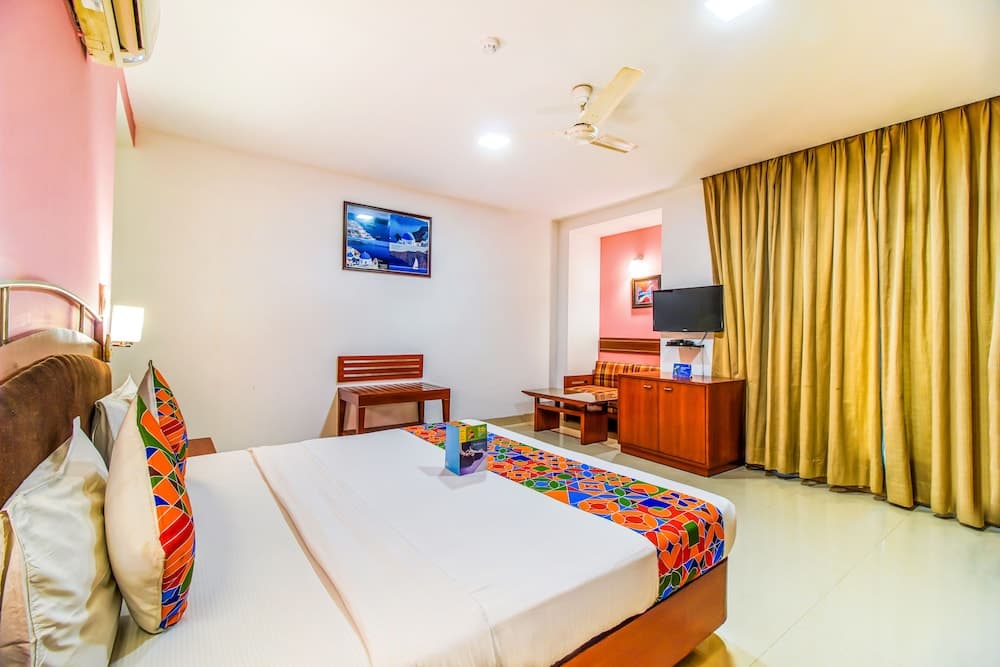 A cozy hotel room features a neatly made bed with colorful bedding, wooden furniture, a flat-screen TV, and warm lighting, ideal for travelers seeking comfort and relaxation.