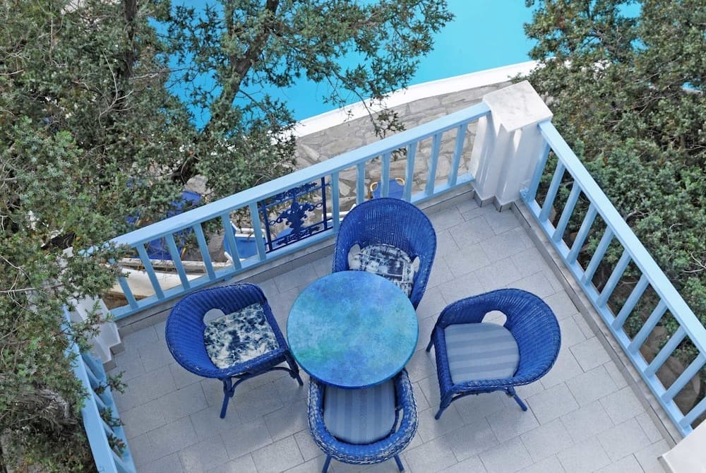 A serene balcony with blue wicker furniture overlooks lush greenery and a tranquil pool, ideal for a relaxing vacation retreat.