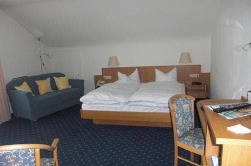 A cozy hotel room features a neatly made bed, a comfortable sofa, and a wooden desk, creating a welcoming atmosphere ideal for travelers seeking relaxation and convenience.