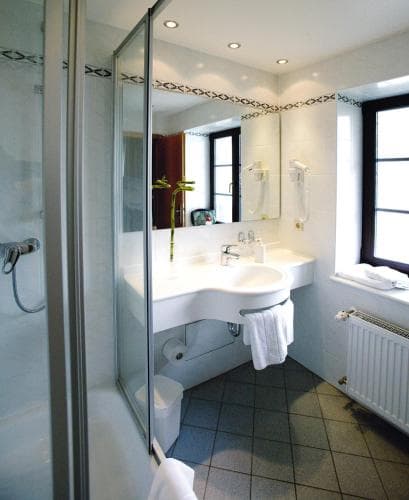 A cozy hotel bathroom features a sleek glass shower, tiled floors, a modern sink with a mirror, and a window letting in natural light, ideal for travelers seeking comfort and cleanliness.
