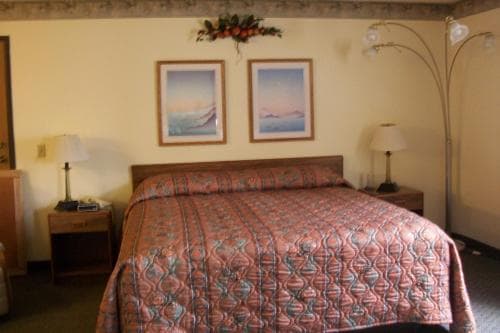 A cozy hotel room features a neatly made bed adorned with a patterned quilt, framed ocean artwork on the walls, and bedside lamps, creating a welcoming atmosphere ideal for travelers seeking comfort and relaxation.