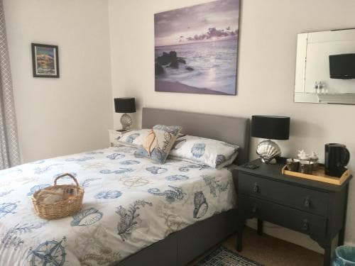 A cozy bedroom with a nautical-themed bedspread, seashell decor, and ocean artwork creates a serene seaside retreat, ideal for travelers seeking relaxation.