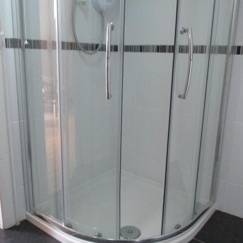 A modern bathroom features a sleek, curved glass shower enclosure with chrome handles, ideal for travelers seeking compact yet stylish accommodations.