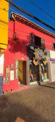 A vibrant red building with colorful decorations and a cheerful café entrance invites travelers to explore its lively street-side charm in a sunny urban setting.