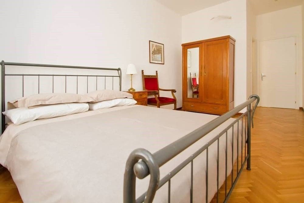A cozy bedroom with a metal bed frame, wooden wardrobe, red armchair, and soft lighting creates a serene atmosphere ideal for travelers seeking a comfortable stay in a minimalist setting.
