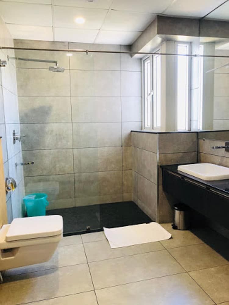A modern bathroom with tiled walls, a walk-in shower, sleek black vanity, and natural light from a window creates a clean and functional space ideal for travelers seeking comfort and convenience.