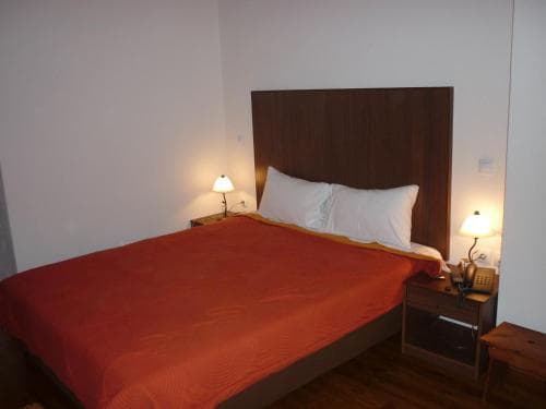 A cozy hotel room features a neatly made bed with a vibrant red duvet, flanked by wooden bedside tables with warm-lit lamps, ideal for travelers seeking comfort and simplicity.