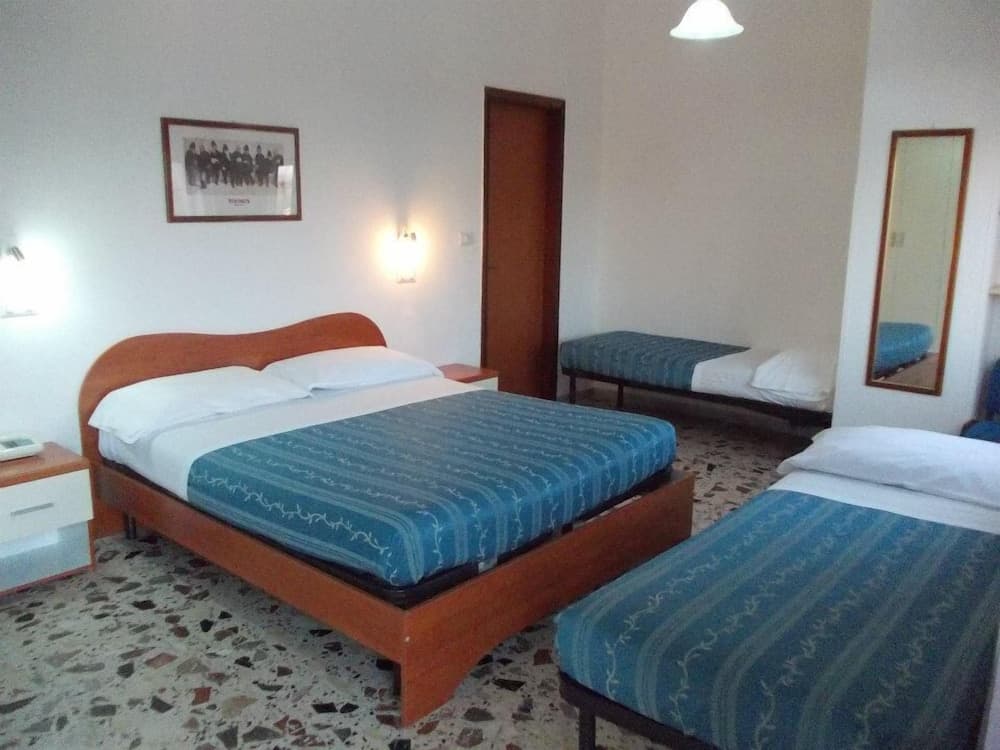 A cozy hotel room with wooden beds adorned in blue striped bedding, a speckled floor, and simple decor offers a comfortable stay for travelers seeking relaxation.