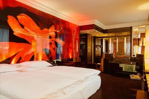 A vibrant hotel room features a bold orange mural, plush bedding, and modern furnishings, creating an inviting atmosphere ideal for travelers seeking a stylish and comfortable stay.