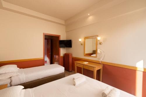 A cozy hotel room with two neatly made beds, warm lighting, a wooden desk, and a mounted TV, ideal for travelers seeking comfort and simplicity during their stay.