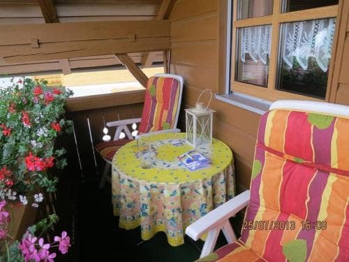 A cozy balcony adorned with vibrant striped chairs, a floral tablecloth-covered table, and lush potted flowers creates an inviting atmosphere perfect for a relaxing getaway or vacation rental retreat.