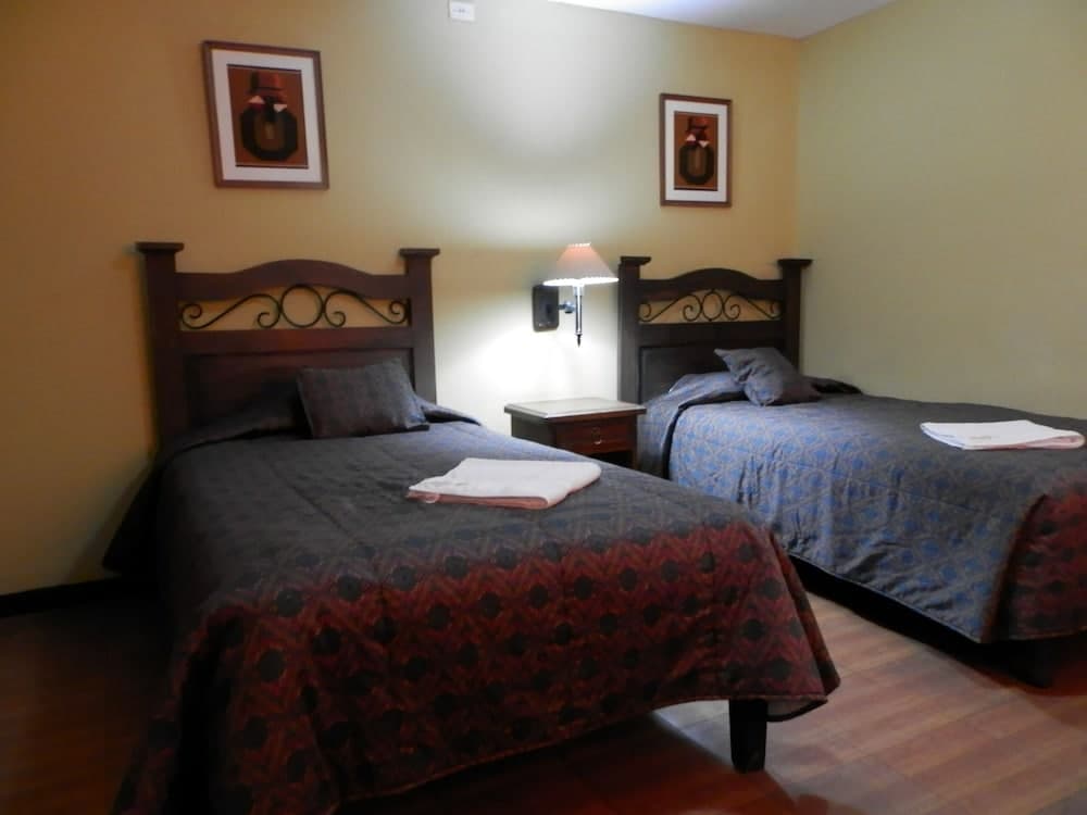 A cozy hotel room features two neatly made beds with patterned quilts, framed artwork on the walls, and a warm ambiance ideal for travelers seeking comfort and relaxation.