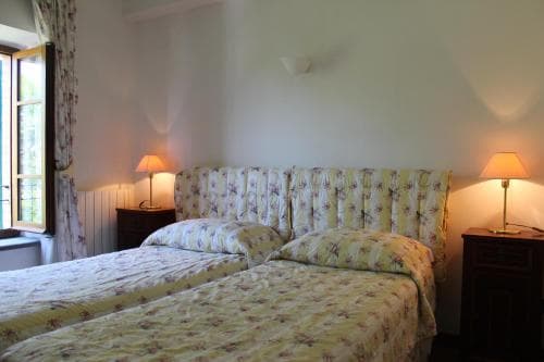A cozy hotel room features twin beds with floral bedding, warm bedside lamps, and a window with curtains, ideal for travelers seeking a comfortable and inviting stay.